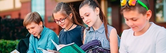 Quatro crianças sentadas lado a lado lendo seus livros